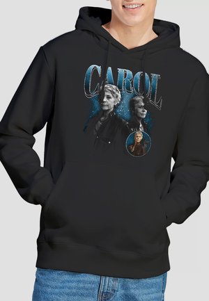 Schwarzer Hoodie mit zwei älteren Frauen und einem kleineren runden Porträt darunter, darüber das Wort „CAROL“ in großen blauen Buchstaben.
