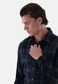 Camicia a quadri blu e verde realizzata in tessuto morbido, caratterizzata da un colletto classico e una pattina con bottoni, con una vestibilità regolare e maniche lunghe.