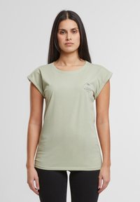 Hellgrünes T-Shirt mit aufgerollten Kurzarm, rundem Halsausschnitt und einem kleinen Druck eines Palmbaums auf der linken Brustseite. Weicher Stoff.