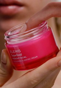 Bocal en verre rose de la crème de nuit nourrissante ELEMIS Superfood Midnight Facial. Le couvercle est transparent, et un doigt plonge dans la crème.