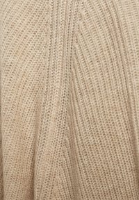 Beżowa dzianina o prążkowanej fakturze, z pionowymi liniami i subtelnymi różnicami kolorystycznymi, tworząca miękki, ciepły wygląd.