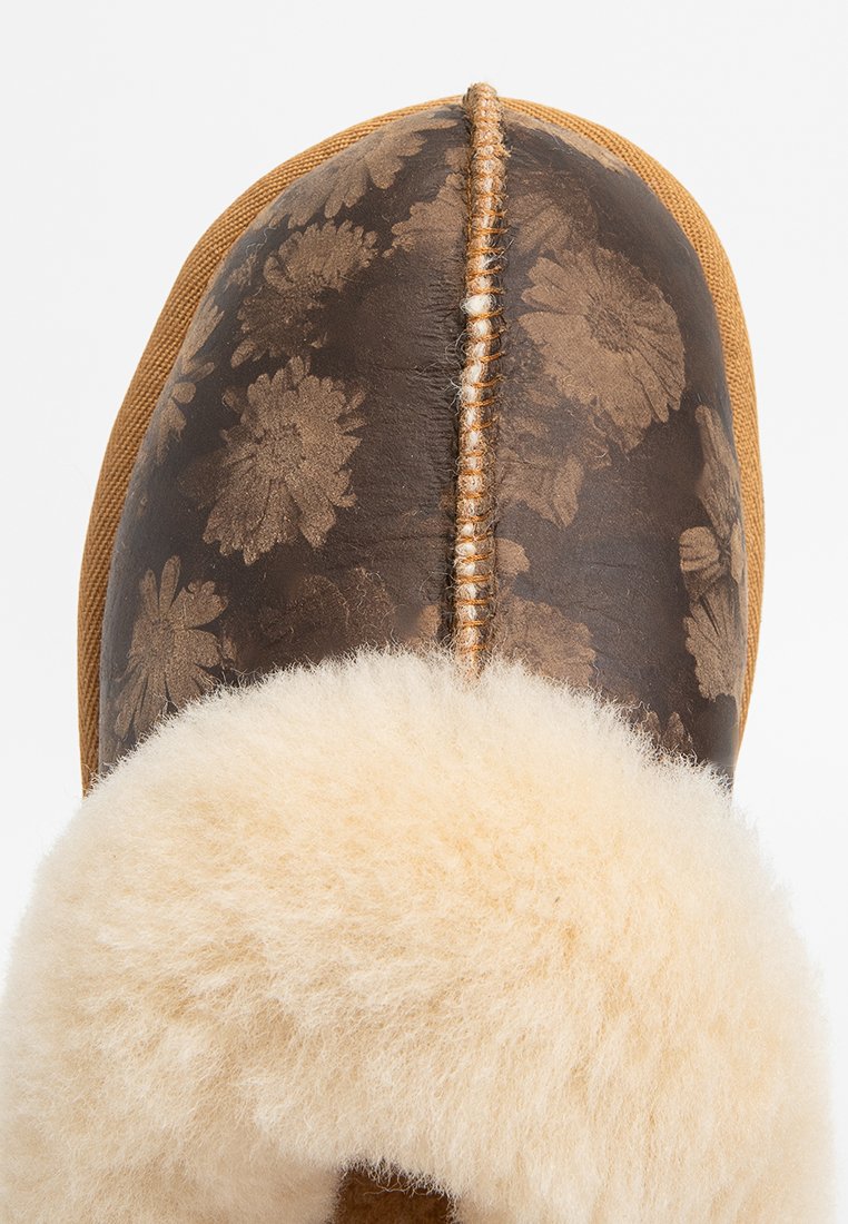 Bruine lederen slippers met bloemmotief, beige bontvoering en tan accenten. Heeft een centrale naad en een gestructureerde afwerking.