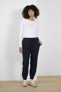 Bílý dlouhý rukáv top spárovaný s tmavě námořnickými jogger kalhotami s elastickými manžetami a bočními kapsami. Modelka má na sobě světlé tenisky.