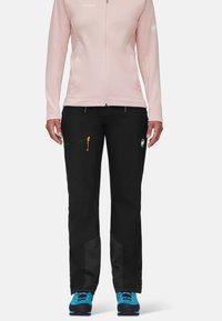 Czarne spodnie z bocznymi kieszeniami na suwak, pomarańczowymi suwakami i chropowatymi czarnymi panelami. Połączone z jasnoróżową kurtką na suwak. Widoczne niebieskie obuwie.