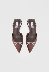 Tacones altos de satén marrón con tiras traseras, de punta afilada, adornados con un lazo de strass, que presentan un diseño elegante y una textura suave.