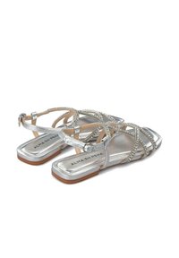 Srebrne płaskie sandały z krzyżującymi się paskami ozdobionymi cyrkoniami, z kwadratowym noskiem i jasnobrązową gumową podeszwą.