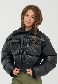 Giacca a vento cropped nera con colletto alto, zip frontale e due tasche sul petto. Texture in finta pelle liscia con polsini a costine.