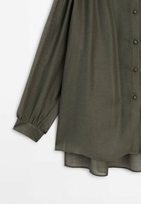 Dark green, lightweight blouse with long, puffed sleeves, front button closure, and a curved hem. Smooth texture with a sheer overlay detail.