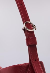 Cinghia a spalla in pelle rossa con cuciture rosse chiare, dotata di un gancio in metallo argentato e di una fibbia regolabile per l'adattamento della lunghezza.