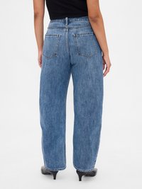 Jeans de mezclilla azul de tiro alto con un ajuste holgado, que cuentan con bolsillos traseros y detalles de costura, combinados con botas negras de tacón.
