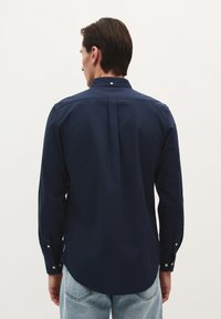 Marineblaues Langarmhemd aus Baumwollstoff, mit klassischem Kragen, Rückenfalte und geknöpften Manschetten. Glatte Textur und taillierte Passform.