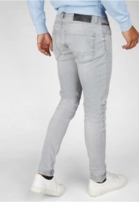 Jeans in denim grigio chiaro con una vestibilità slim, dotati di tasche posteriori e dettaglio della cintura nera. Abbinati a sneakers bianche basse.