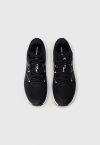 Chaussures de sport noires avec une tige en mesh, semelle blanche rembourrée et lacets noirs. Comprend des accents et des lettres argentés sur la languette et les côtés.