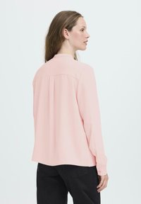 Helles rosa Langarmbluse mit Kragen, ausgestattet mit einem Rückenschlitz und geknöpften Manschetten. Glatte Textur und lässige Passform.