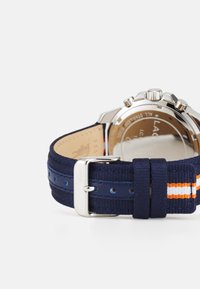 Correa de reloj textil azul marino con rayas naranjas y blancas, hebilla y costuras en tono plateado, que presenta un acabado texturizado y una esfera de reloj redonda.