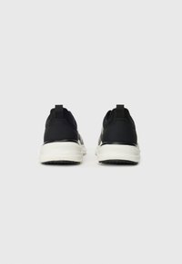 Chaussures de sport noires avec une tige lisse, une semelle intermédiaire blanche contrastante, une semelle extérieure noire texturée et une languette au talon pour un enfilage facile.