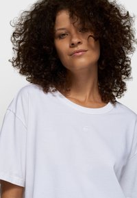 Hvid bomuld t-shirt med rund halsudskæring og korte ærmer, med et diskret broderet logo på brystet. Blød tekstur og afslappet pasform.