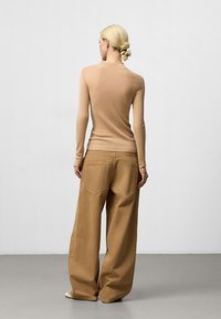 Pull en maille beige à col roulé avec des manches longues, associé à un pantalon beige ample avec des poches arrière et une coupe droite.