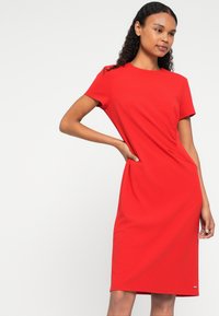 Piros, térd felett érő ruhák rövid ujjakkal, oldalán redős részlettel a textúra fokozásáért; sima, rugalmas anyagból készült.