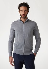 Maglione grigio con zip e colletto alto, realizzato in materiale morbido. Presenta maniche lunghe e polsini a coste, progettato per un look aderente.