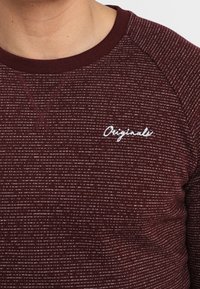 Weinrotes Sweatshirt mit langen Ärmeln, strukturiertem Rippmuster und weißem "Originals"-Logo auf der Brust. Rundhalsausschnitt mit kontrastierendem Besatz.