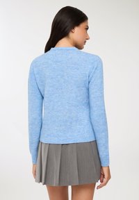Maglione lavorato a maglia di colore blu chiaro con scollatura rotonda, maniche lunghe e orlo a coste. Abbinato a una gonna grigia plissettata.