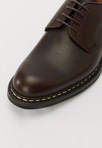 Brun læder sko med rund tå, snørebåndsdesign, synlig syning og en tekstureret sort sål med cremefarvet accent-syning.