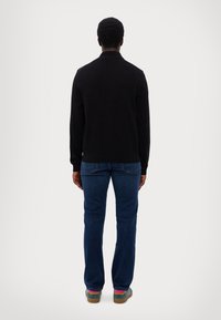 Black long-sleeve sweater with a collar, worn with blue denim jeans and green and pink-accented shoes, viewed from the back.