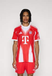Maillot de football rouge et blanc avec des rayures verticales, présentant un logo sur la poitrine, un graphique en forme de T et des manches courtes. Assorti à un short rouge.