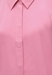 Ροζ πουκάμισο με γιακά και κρυφά κουμπιά στο μπροστινό μέρος, κατασκευασμένο από λείο ύφασμα.