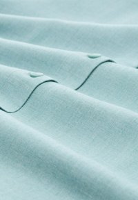 Tejido azul claro con textura suave, que presenta ondas sutiles y dos botones de plástico. El material parece suave y ligero.