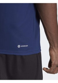 T-shirt de sport bleu marine en tissu respirant, avec un motif texturé et le logo Aeroready près de l'ourlet. Shorts noirs visibles.