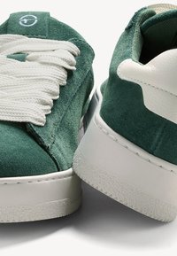 Sneaker verde in suede con dettagli in pelle bianca, spesse stringhe bianche e una suola in gomma testurizzata con un motivo a diamante.
