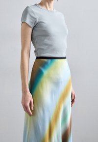 Haut gris clair à manches courtes côtelé associé à une longue jupe présentant un motif dégradé coloré de bleu, marron et jaune avec une ceinture noire.