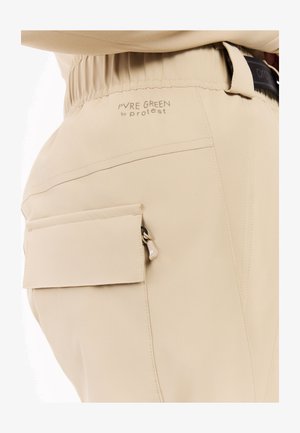 Beige windbreakerbroek met elastische tailleband en een zijritszak. Heeft een gladde textuur en subtiele branding op de achterkant. Lichtgewicht ontwerp.