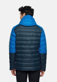 Giacca imbottita di un blu scuro con accenti blu brillante. Presenta un cappuccio e un design trapuntato con blocchi di colore a contrasto sulle spalle.