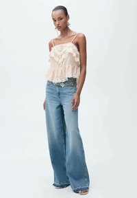 Svijetloružičasti top s ruffles detaljima i čipkastim naglascima, uparen s svijetloplavim širokim trapericama. Jednostavne sandale upotpunjuju outfit.