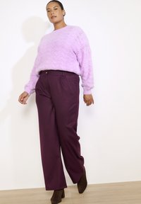 Heled lilla kootud sviiter lainemustriga, millega on kombineeritud sügava lilla avara lõikega püksid, millel on õhukesed vertikaalsed triibud. Väljanägemist täiustavad pruunid kontsakingad.