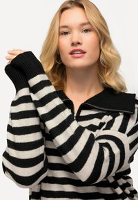 Schwarzer und cremefarbener gestreifter Pullover mit einem Reißverschlusskragen, gerippten Bündchen und einer weichen Textur; hat breite horizontale Streifen.