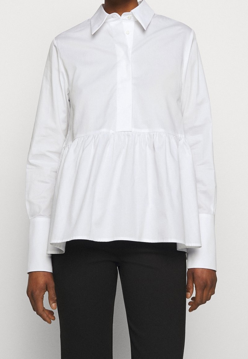 Camisa blanca de manga larga con botonadura en el frente, que presenta una cintura plisada y un cuello estructurado; tejido suave con un ajuste relajado.