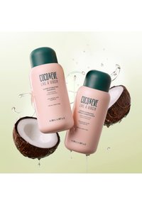 Två rosa flaskor med gröna korkar märkt "Coco & Eve Like a Virgin Super Hydrating Shampoo" och "Balsam", omgivna av kokoshalvor och vattendroppar.