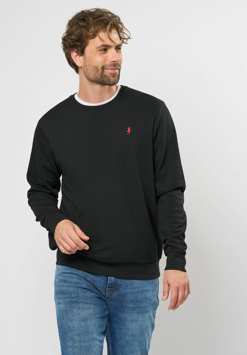 Zwarte sweatshirt met een ronde hals, ribgebreide manchetten en een klein rood logo op de linkerkant van de borst, gecombineerd met blauwe jeans. Soepele stoftextuur.