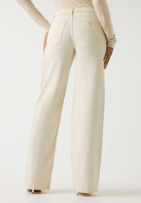 Φαρδιά τζιν σε ανοιχτό μπεζ χρώμα με λεία υφή, διαθέτει ψηλή μέση, δύο πίσω τσέπες και ένα διακριτικό λογότυπο στη μέση.