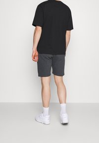 T-shirt noir en coton manches courtes assorti à un short gris en coton. Le modèle porte des baskets blanches et des chaussettes blanches. Tenue simple et décontractée.