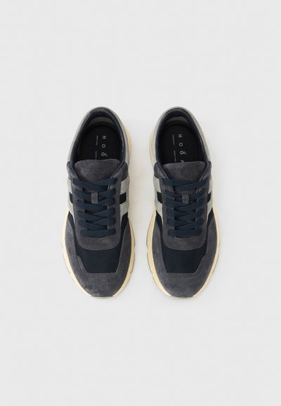 Αθλητικά παπούτσια με επάνω μέρος από σκουρό μπλε και γκρι σουέντ, πάνελ από δίχτυ και μαύρα κορδόνια, με ανοιχτόχρωμη λαστιχένια σόλα και ενσωματωμένη ετικέτα με το λογότυπο.