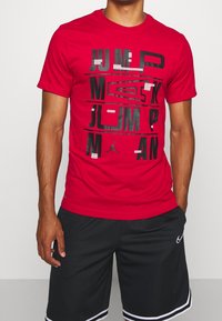 Rode katoenen t-shirt met gedurfde zwarte tekst en "Jumpman" afbeelding. Korte mouwen en ronde halsstijl. Gecombineerd met zwarte shorts.