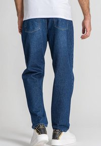 Vaqueros de mezclilla en un tono azul oscuro con un corte relajado, con bolsillos traseros y puños elásticos en el dobladillo. Combinados con zapatillas blancas.