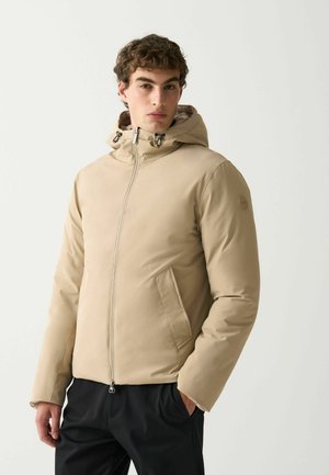 Beige isolerad jacka med dragkedja framsidan, justerbar huva, dragkedjefickor och kontrasterande innertyg; slät textur och strömlinjeformad design.
