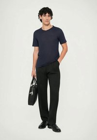 Tamsiai mėlynas trumpomis rankovėmis marškinėlis derinamas su juodomis tiesiomis kelnėmis. Modelis laiko juodą rankinę, vilki juodus batelius ant šviesios fono.