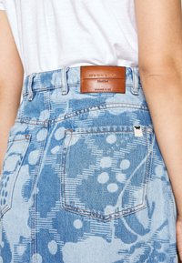 Shorts de mezclilla en azul claro con un diseño estampado. Presentan una etiqueta de cuero marrón en la cintura y detalles de bolsillo estándar.